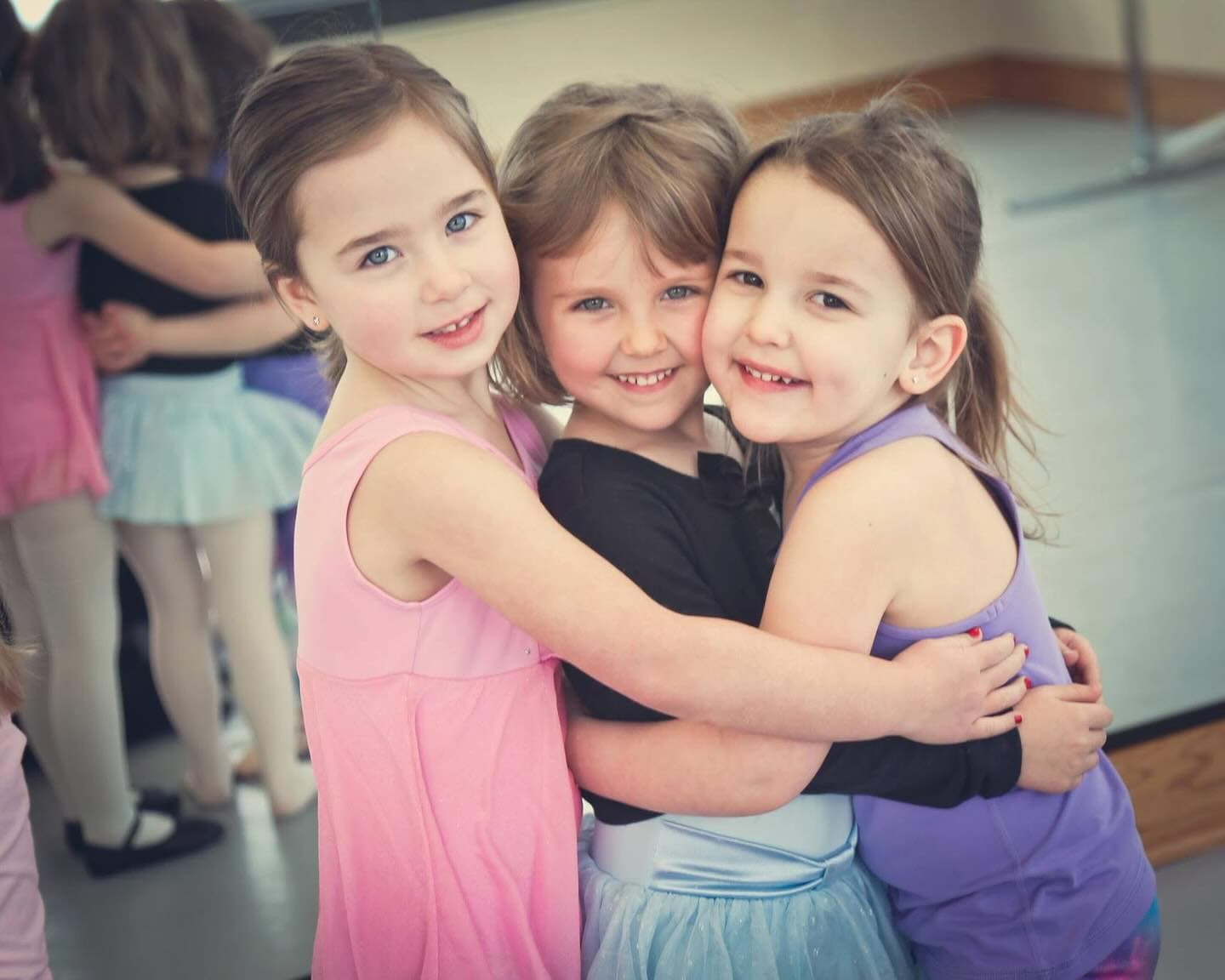 Three young dancers hugging and smiling at The Dance Company studio